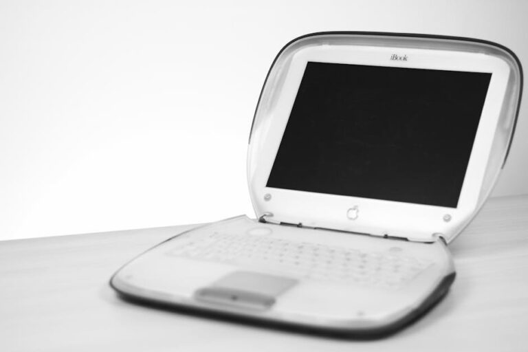 Classic iBook laptop with keyboard and screen displayed on a desk in monochrome.