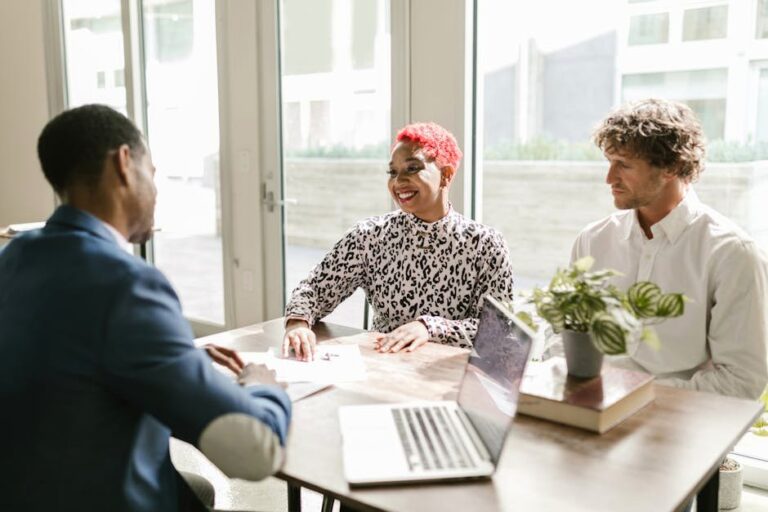 Three professionals meeting in a sunny office discussing finance with smiles.