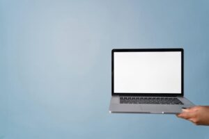 A person holding a laptop with a blank screen against a blue background, perfect for mockups.