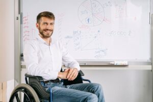 Smiling man in wheelchair at office, presenting business graphs on whiteboard