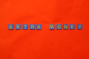 Bright orange background with 'EXTRA MONEY' spelled in blue and yellow tiles, illustrating financial concepts.