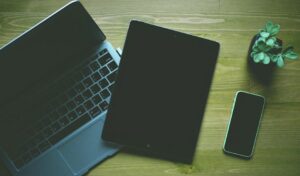 A top-down view of a workspace featuring a laptop, tablet, smartphone, and a small plant.