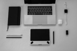Black and white flatlay of stylish tech gadgets including laptop and smartwatch on a desk.
