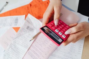Hands using a pink calculator to manage expenses amidst various receipts and documents.