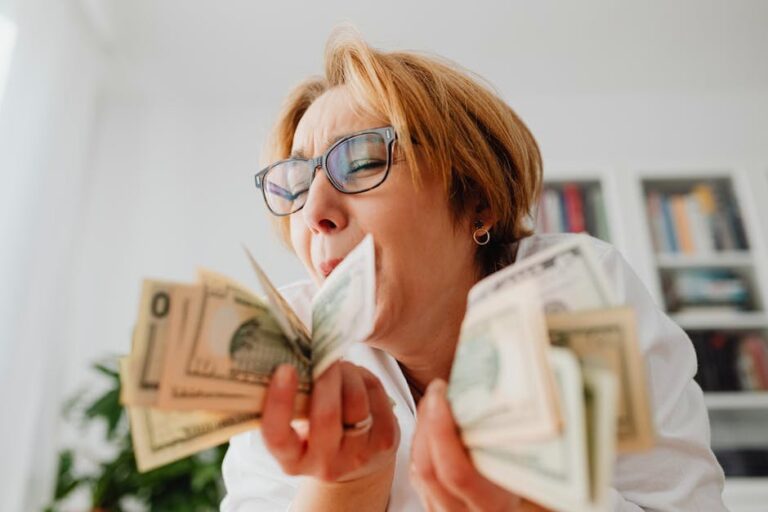 A happy woman with eyeglasses cherishing US dollar bills indoors, symbolizing wealth and financial success.