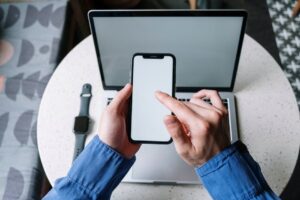 Hands operating a smartphone above a laptop with a smartwatch nearby, showcasing modern technology.