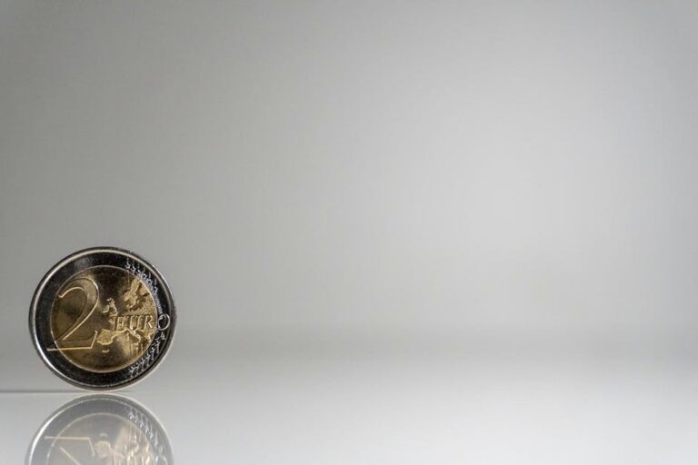 A single 2 Euro coin standing on a reflective surface against a plain background.