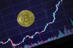 Gold Bitcoin on screen with rising investment chart indicating cryptocurrency growth.