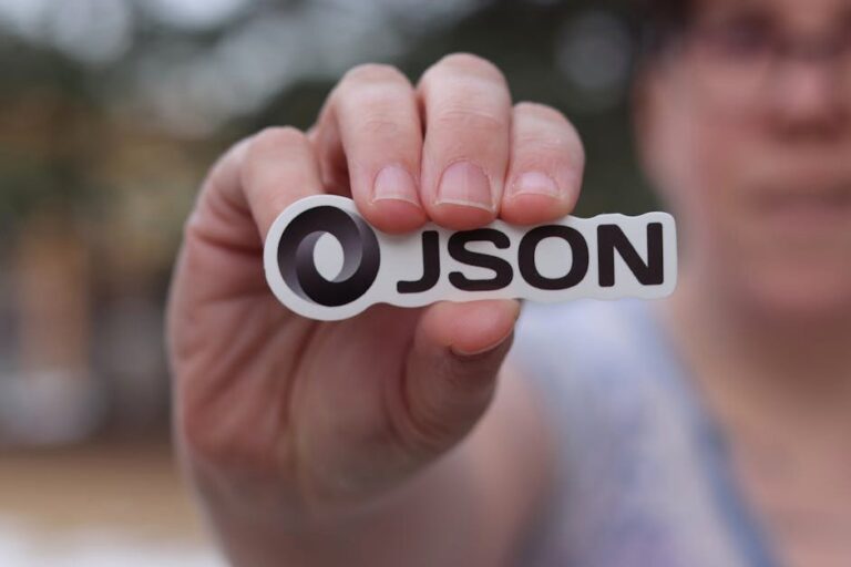 A close-up of a hand holding a JSON logo sticker outdoors, blurred background.