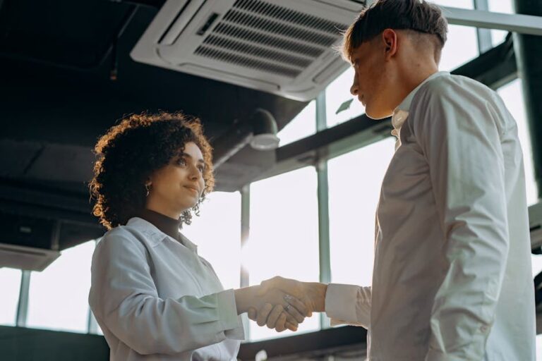 Business professionals exchange a handshake in a modern office setting, symbolizing collaboration.