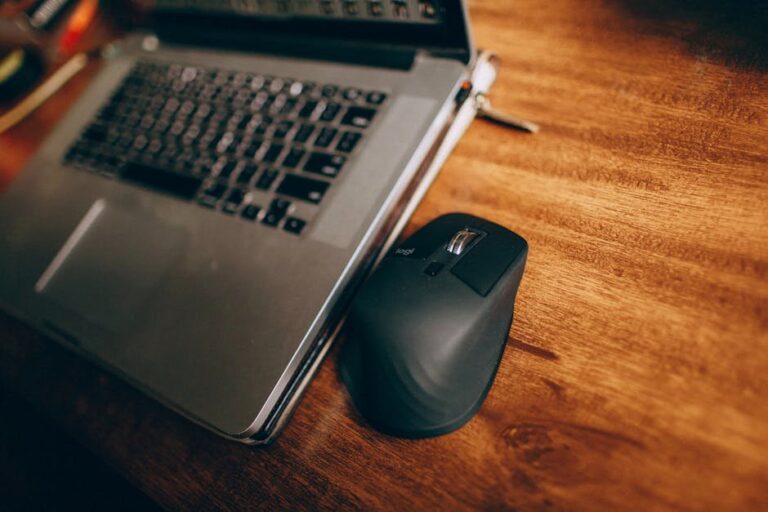 Close-up of a wireless mouse and laptop on a wooden desk, ideal for tech and workspace concepts.