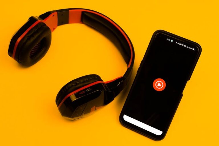Wireless headphones and smartphone with play icon on a vibrant yellow background.