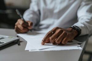 Close-up of a professional writing on documents at a work desk with a laptop.