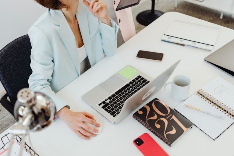 Overhead view of a woman working at an organized desk with a laptop, notebooks, and coffee.