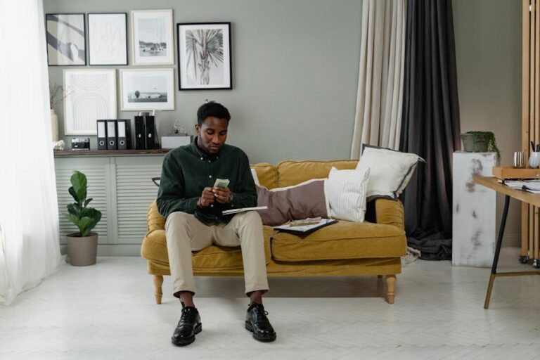 Professional man counting cash, seated on a sofa in a modern and minimalist home office setting.