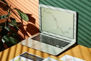 Laptop displaying a financial graph with reports, in a sunlit workspace.