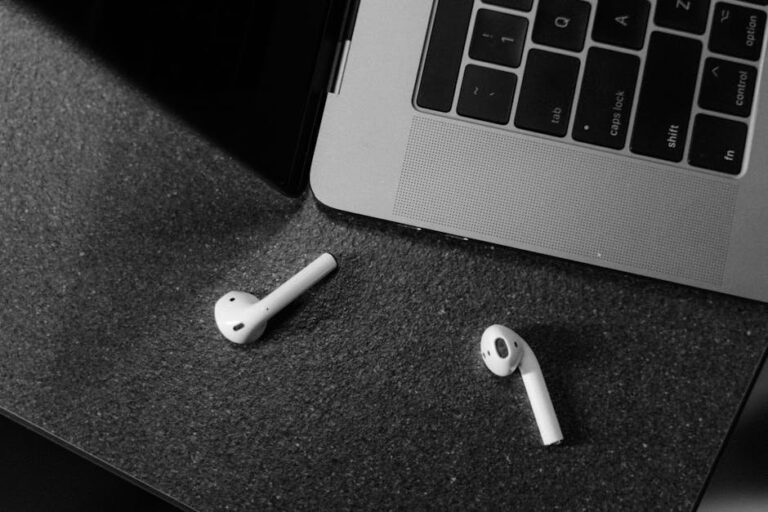 Black and white image of wireless earbuds and laptop, top view.