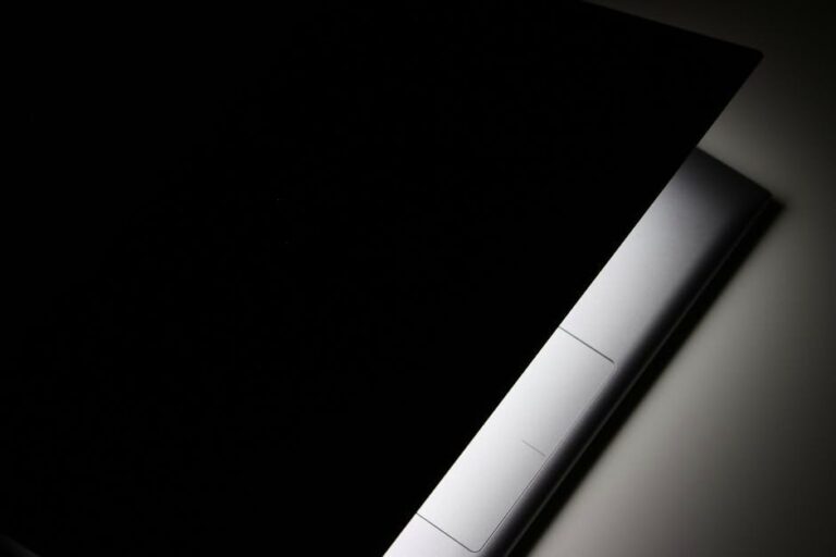 A partial view of a modern laptop closed in shadow, highlighting its sleek design.