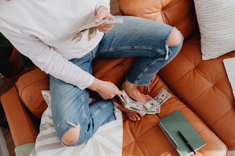 Adult woman sitting on a couch, counting dollar bills with relaxed posture.