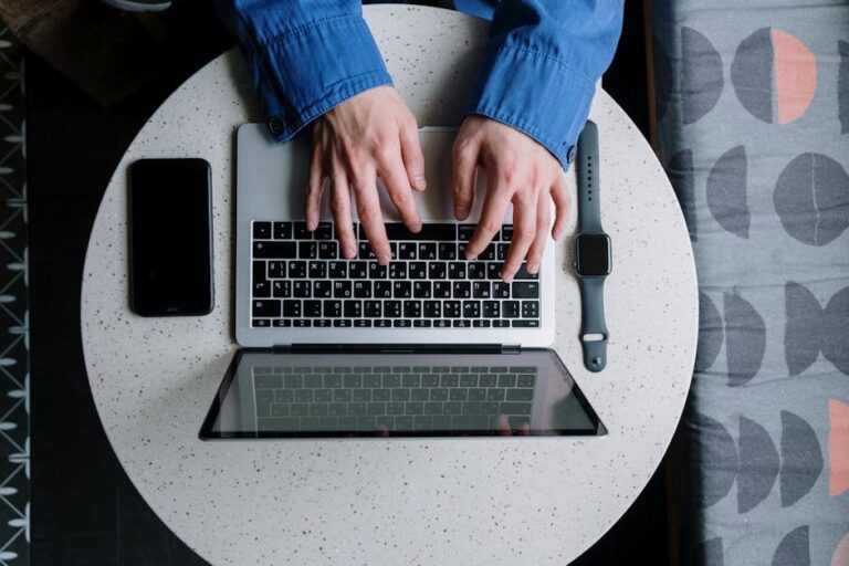 Casual setting with hands typing on a laptop, accompanied by a smartwatch and smartphone.