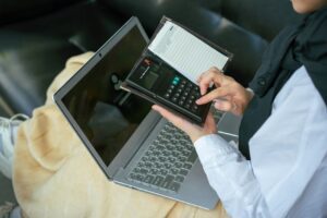 Close-up of a person using a calculator with a laptop, symbolizing home office productivity.