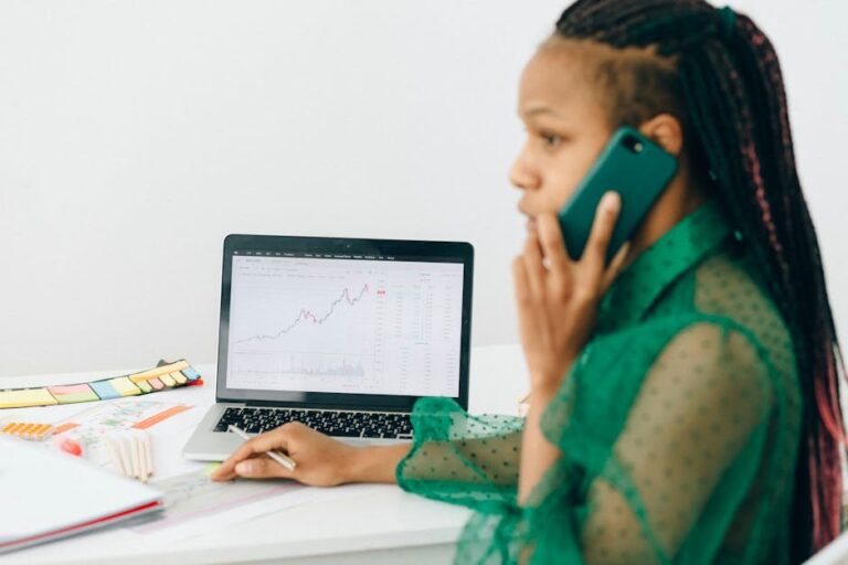 African American woman reviewing stock market charts on a laptop while talking on the phone.
