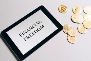Tablet showing 'Financial Freedom' with gold bitcoins nearby, symbolizing cryptocurrency investment.