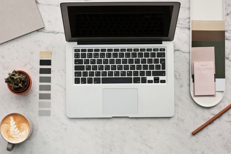 Top view of a stylish workspace featuring a laptop, latte, cactus, and color swatches on a marble surface.