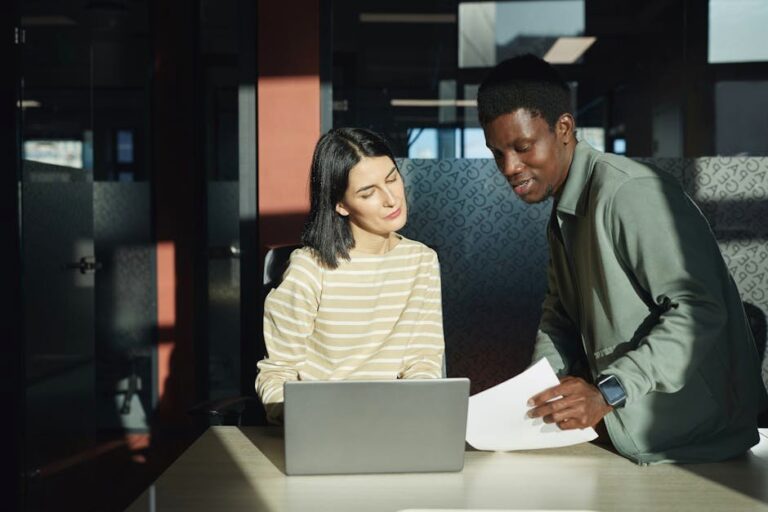 Two professionals discussing work over a laptop in a bright, modern office setting.