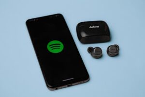 Closeup of Jabra true wireless earbuds with a smartphone displaying the Spotify app on a blue background.