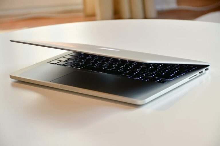 A modern MacBook laptop with a sleek design, slightly closed on a white table indoors.