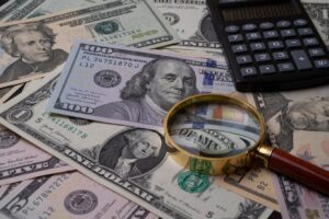 US currency bills with magnifying glass and calculator, symbolizing financial analysis.