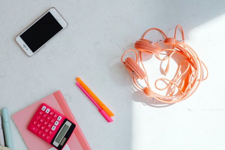 Overhead view of a minimalist desktop with headphones, smartphone, and stationery items on a white surface.
