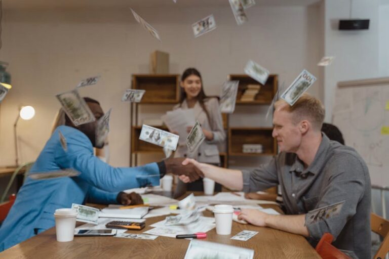 Business professionals handshake amid money falling, symbolizing financial success.