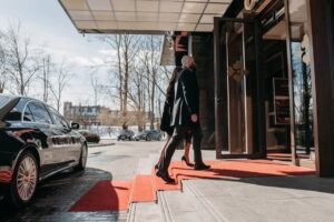 A man and woman elegantly dressed enter a luxury hotel, walking on a red carpet.