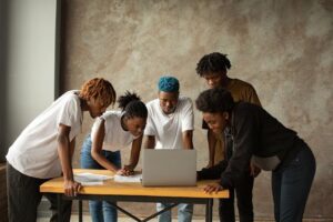 A group of young adults collaborate around a laptop, conveying teamwork and innovation indoors.