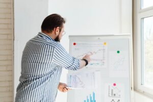 A businessman pointing at financial charts on a whiteboard, discussing stock market trends.