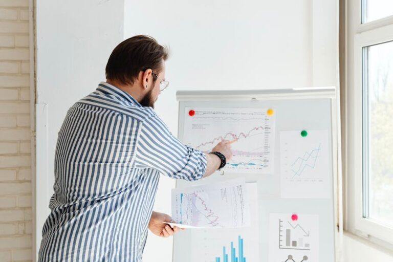 A businessman pointing at financial charts on a whiteboard, discussing stock market trends.