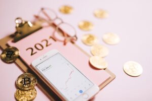 Close-up of a smartphone with crypto chart, bitcoin coins, and 2021 notepad.