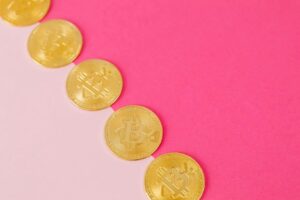Array of gold bitcoin coins on a striking pink surface, symbolizing modern digital currency.