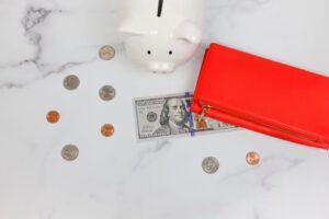 Overhead view of piggy bank, red wallet, and US dollars on marble surface.
