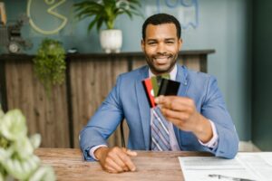Smiling African American man in a suit holding credit cards at a business desk.