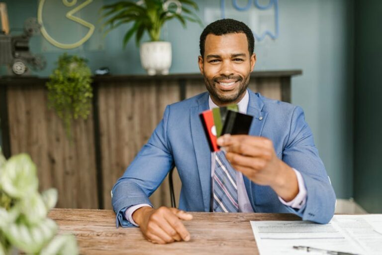 Smiling African American man in a suit holding credit cards at a business desk.