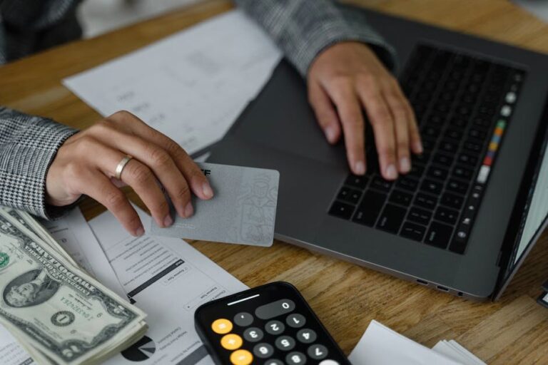 Close-up of a person using a credit card and laptop in a financial setting with cash and calculator.