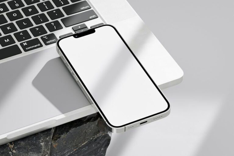 Close-up of a smartphone resting on a laptop with a blank screen for mockup use.