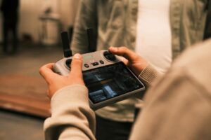 Close-up of a man using a handheld remote controller for drone operation indoors.