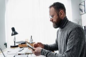 Adult male reviewing documents at a desk with a modern setup, conveying focus and concentration.