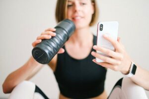 Woman checks smartphone while hydrating with sports bottle during a home workout.