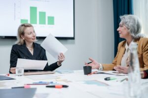 Two businesswomen engaged in a meeting discussing charts in an office setting.