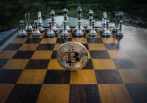 Bitcoin coin standing on a chessboard with silver and brass chess pieces. Concept of strategic digital currency investment.